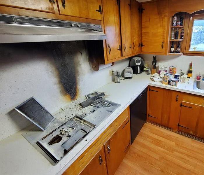 Kitchen fire damage showing destroyed stove, range hood, and cabinets